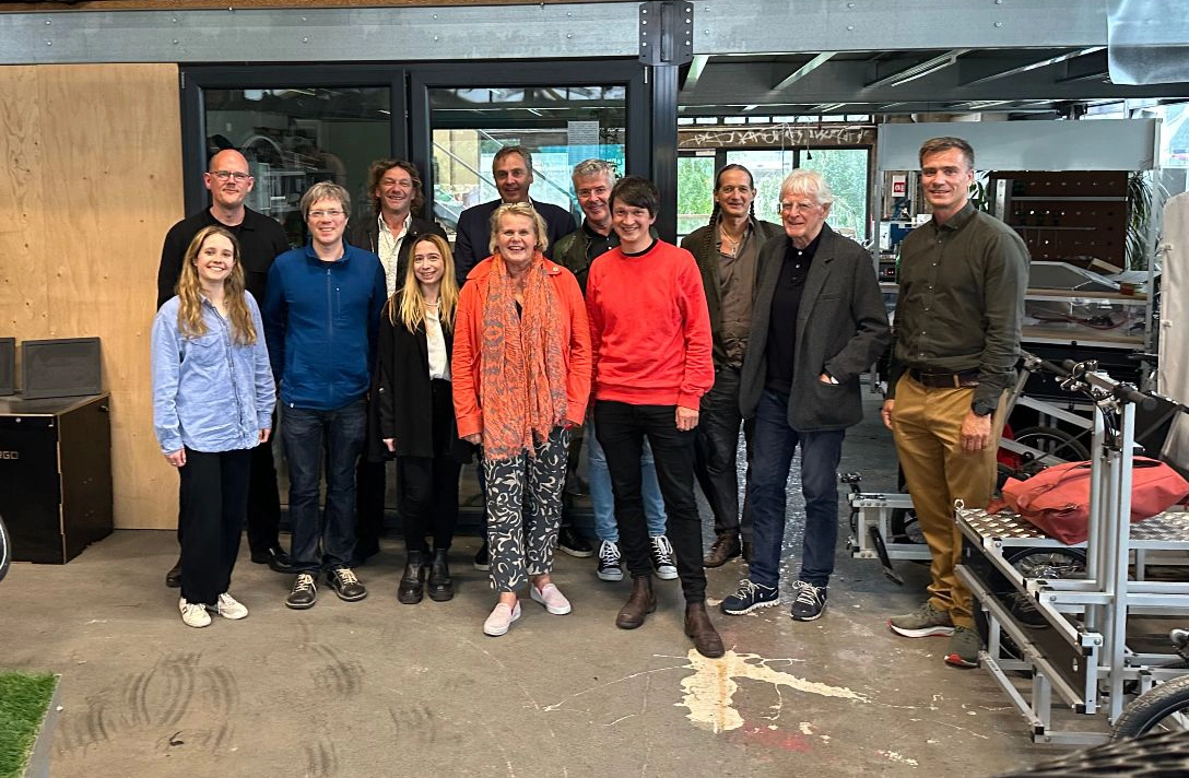 Eine Gruppe von zwölf Personen, dem Wissenschaftlichen Beirat von Fab City Hamburg, steht lächelnd in einem Werkstattraum.