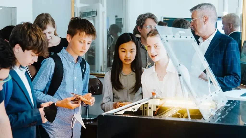 Schüler und Schülerinnen beobachten gespannt eine leuchtende Maschine im Rahmen des Projekts 'Make Your School'.