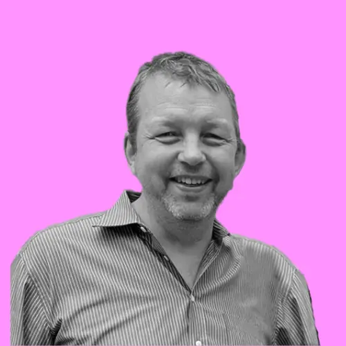 Porträt von Dirk Pieper, einem lächelnden Mann mit Bart und gestreiftem Hemd, vor einem pinkfarbenen Hintergrund.