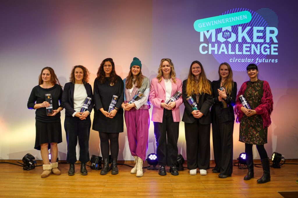 Acht Frauen stehen auf einer Bühne und halten Auszeichnungen der Fab City Maker Challenge in den Händen, mit dem Event-Logo im Hintergrund.