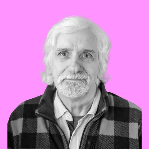 Porträt von Werner Jarmatz, einem älteren Mann mit weißem Haar und Bart, der eine karierte Jacke trägt, vor einem pinkfarbenen Hintergrund.