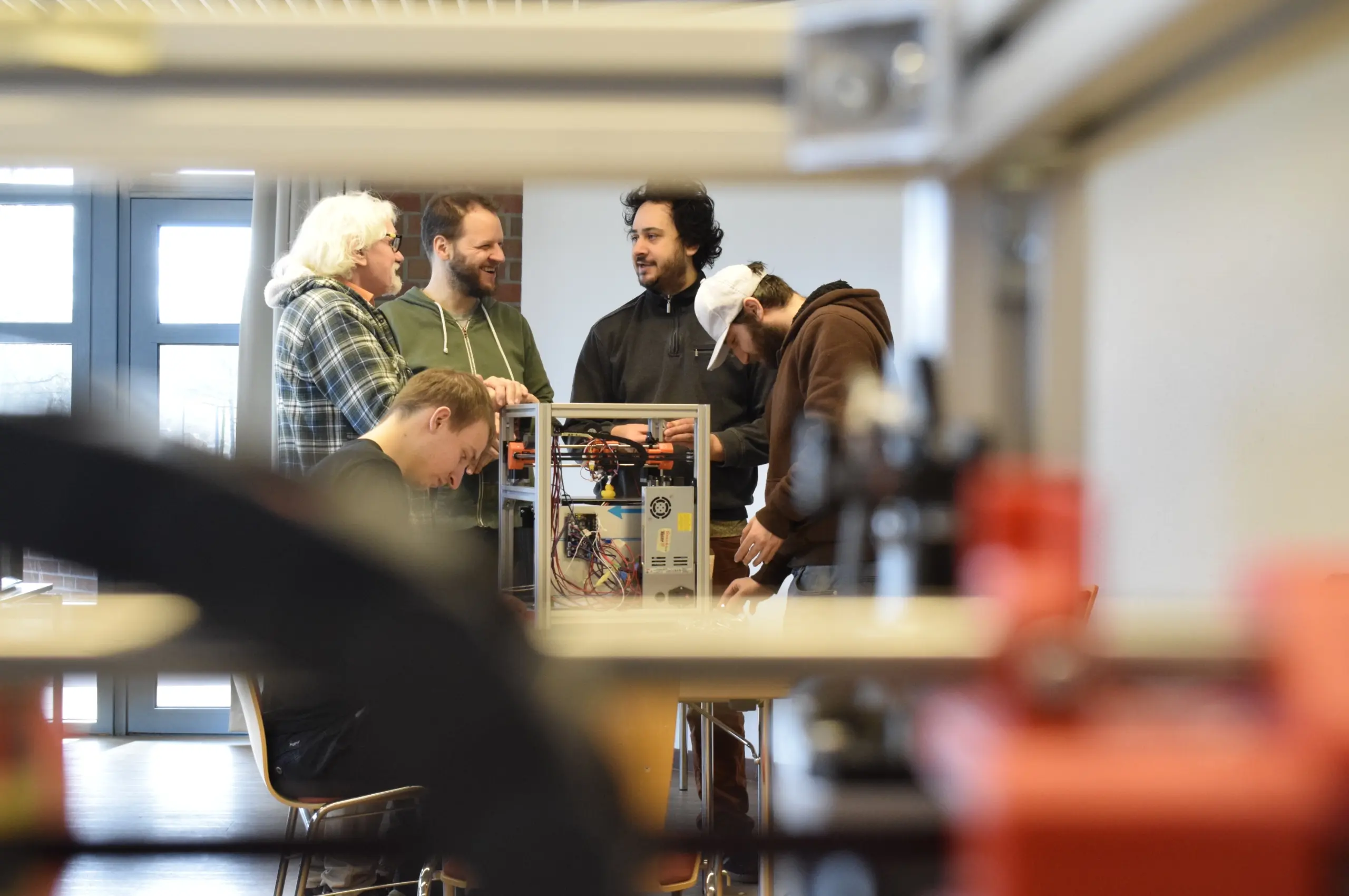 Mehrere Männer arbeiten gemeinsam an einem offenen Gerät, das wie ein 3D-Drucker aussieht, in einem hellen Raum der Fab City Hamburg.